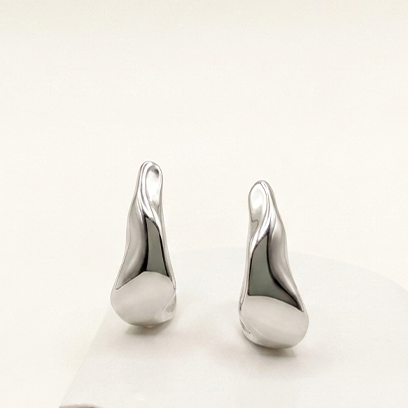 A pair of polished silver abstract-shaped earrings displayed on a white curved stand against a warm off-white background.
