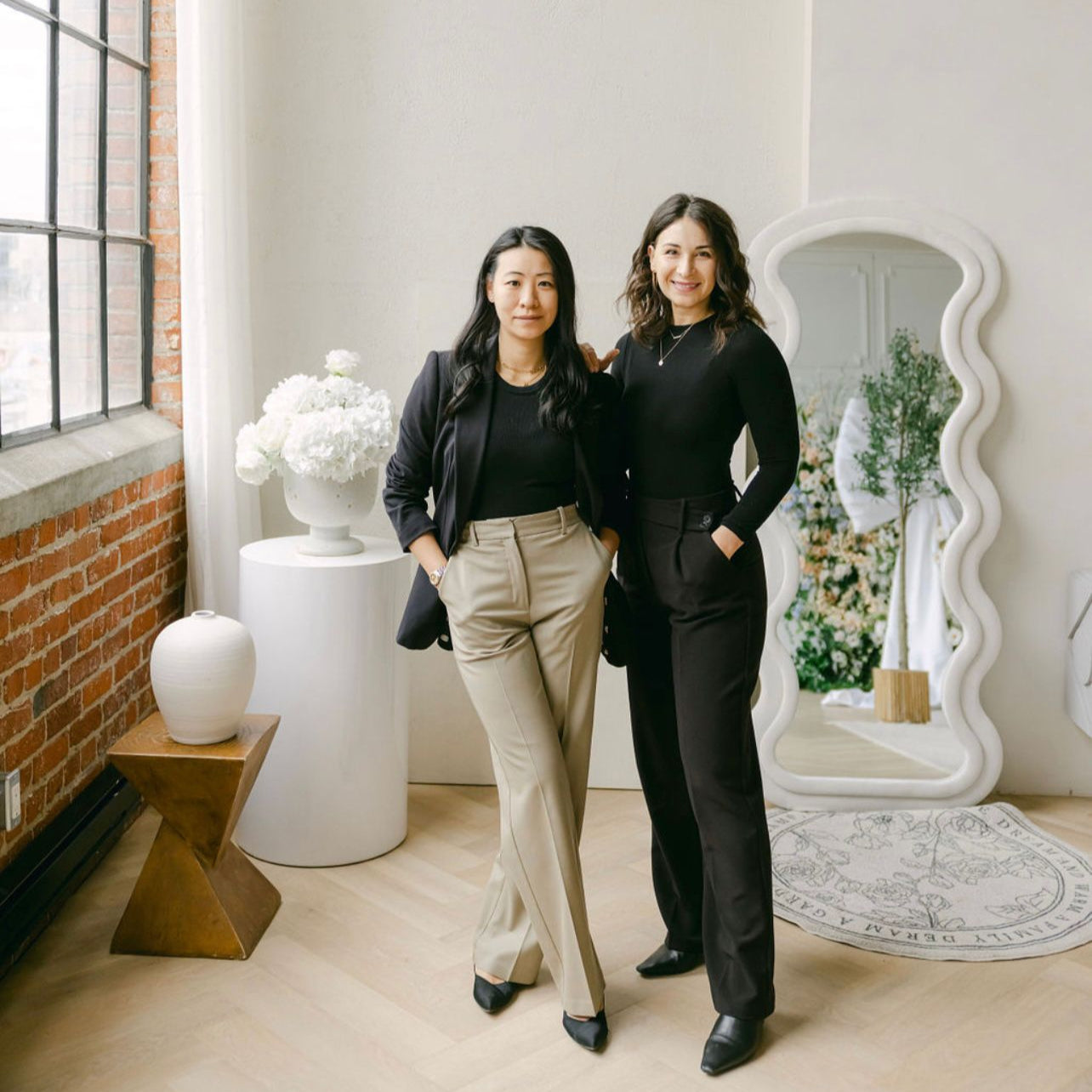 Two women posing together in a stylish interior setting with decor elements.

