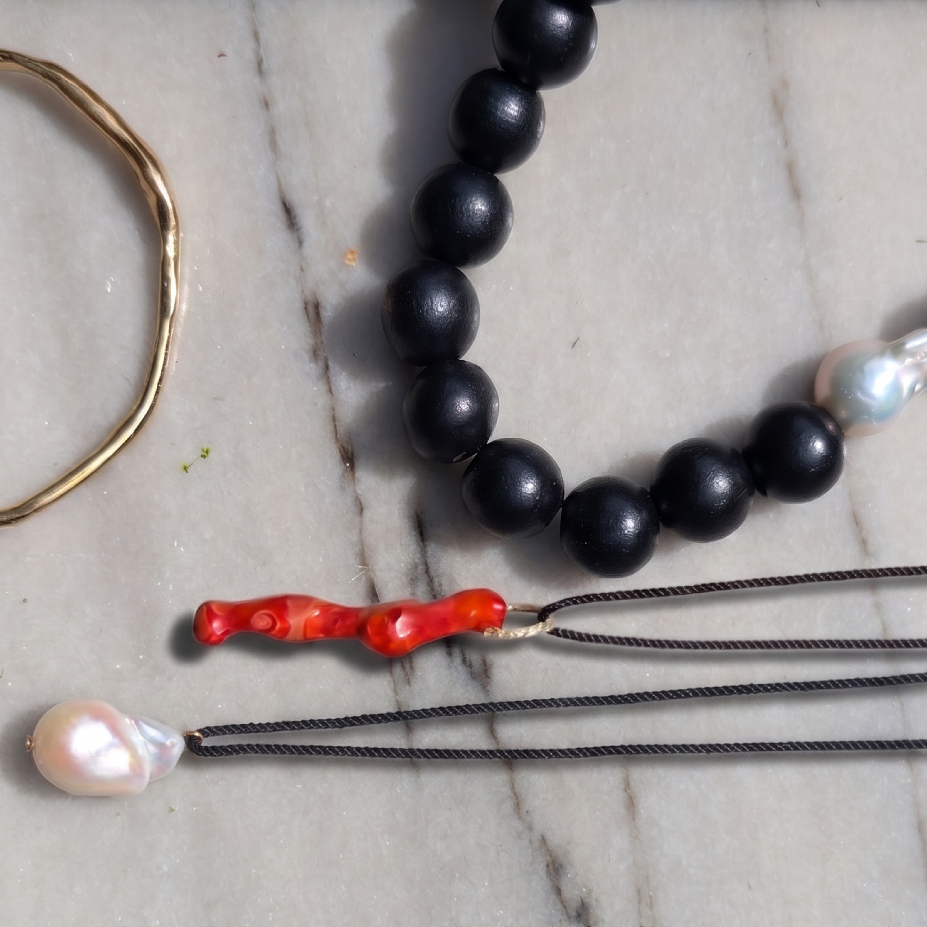 Black beaded necklace with red and pearl accents on a marble surface